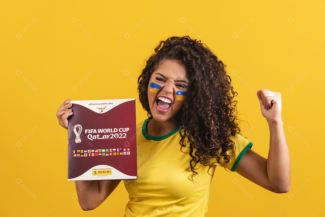 Linda mulher jovem morena segurando álbum da copa do brasil de 2022 futebol cabelo afro sobre fundo isolado amarelo