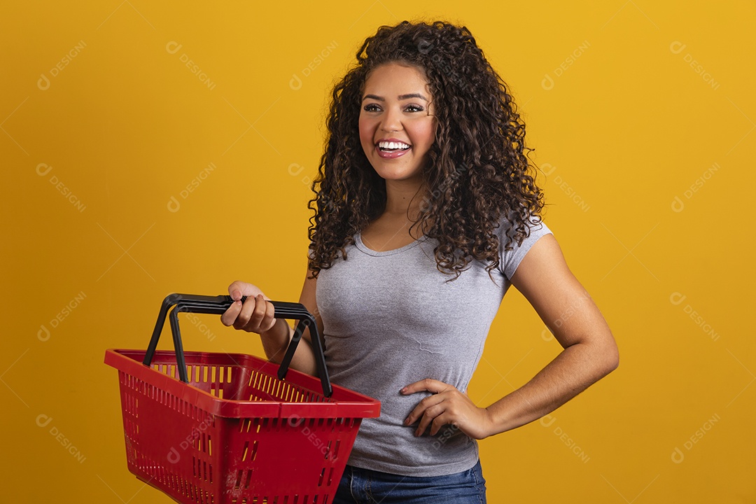Linda mulher jovem morena cabelo cacheado segurando cestas mercado sobre fundo isolado amarelo