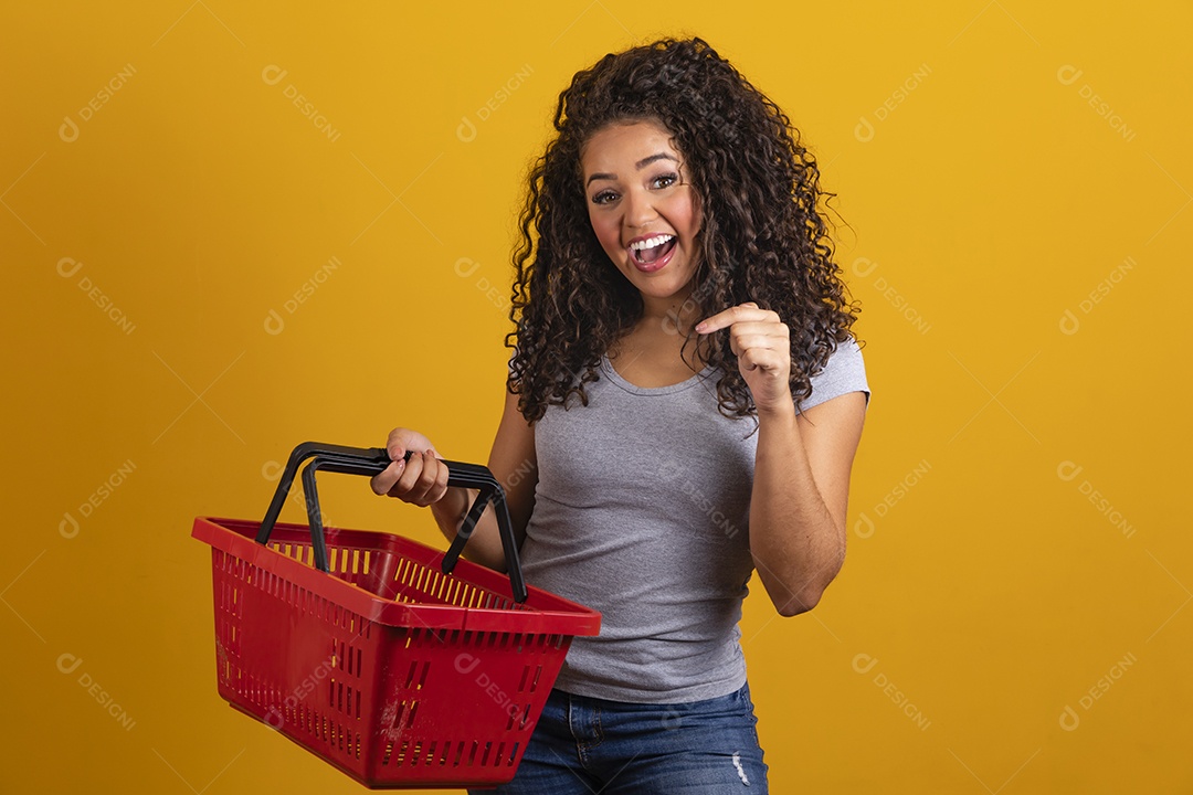 Linda mulher jovem morena cabelo cacheado segurando cestas mercado sobre fundo isolado amarelo