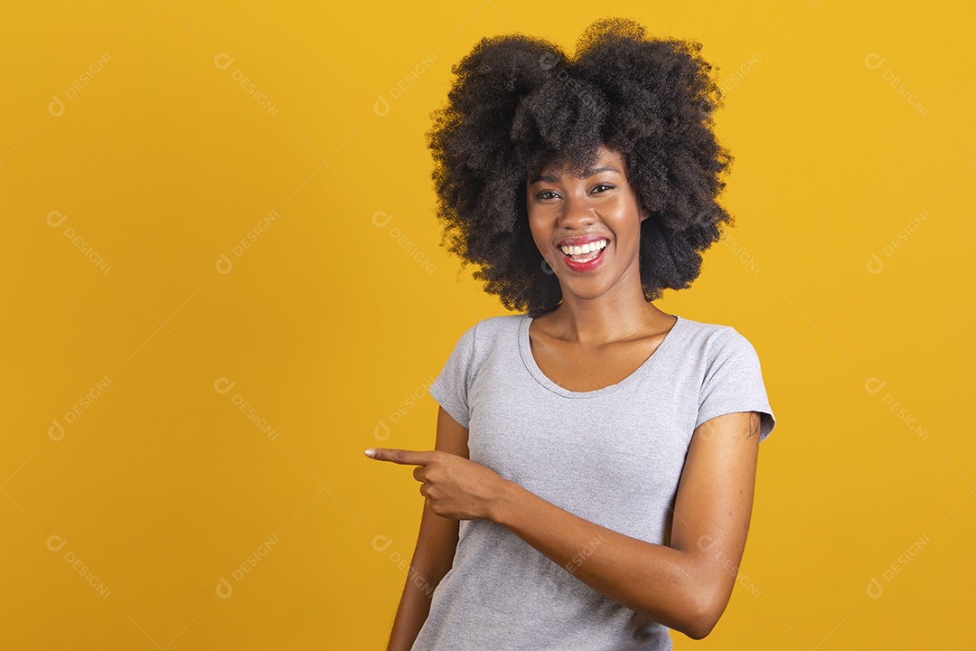Linda mulher jovem morena cabelo afro apontando para lado sobre fundo isolado amarelo