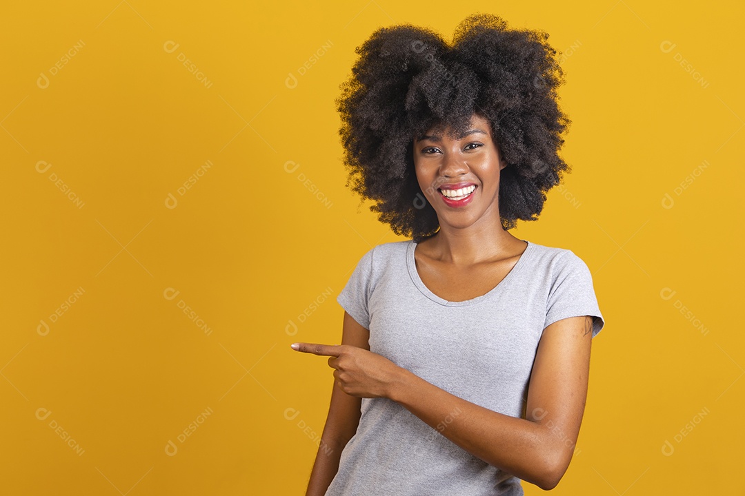 Linda mulher jovem morena cabelo afro apontando para lado sobre fundo isolado amarelo