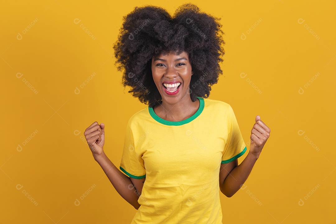 Linda mulher jovem morena torcedora do brasil cabelo afro usando camiseta do brasil sobre fundo isolado amarelo