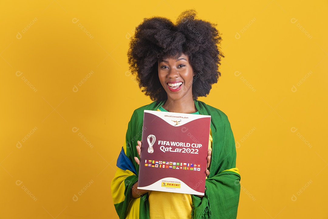 Linda mulher jovem morena segurando álbum da copa do brasil de 2022 futebol cabelo afro sobre fundo isolado amarelo