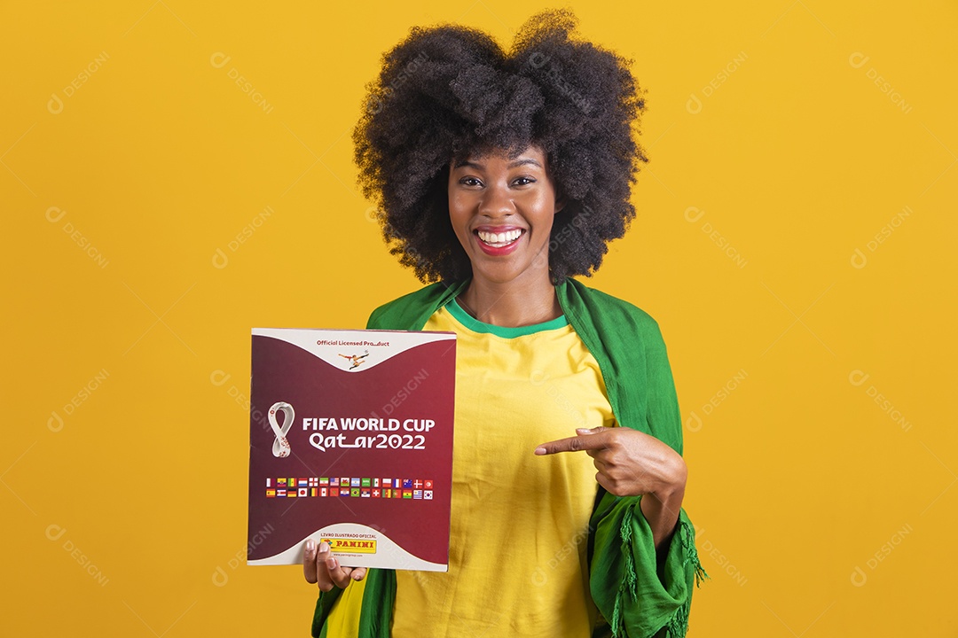 Linda mulher jovem morena segurando álbum da copa do brasil de 2022 futebol cabelo afro sobre fundo isolado amarelo