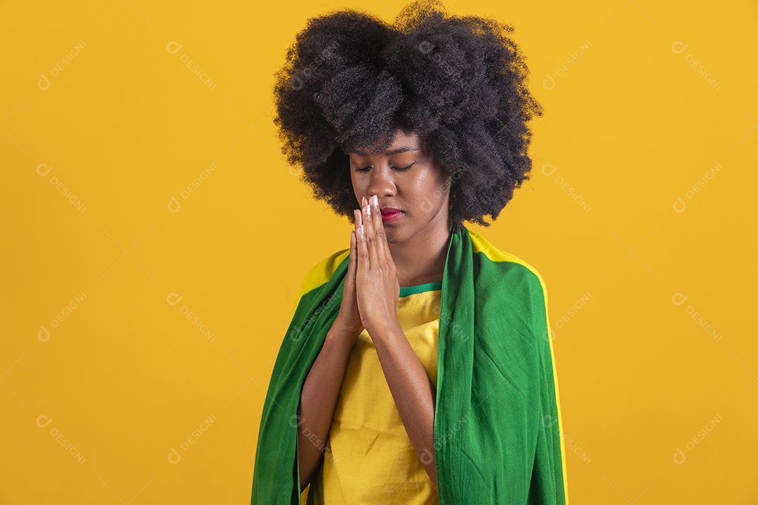 Linda mulher jovem usando camiseta da seleção brasileira morena orando rezando do brasil de 2022 cabelo afro sobre fundo isolado amarelo
