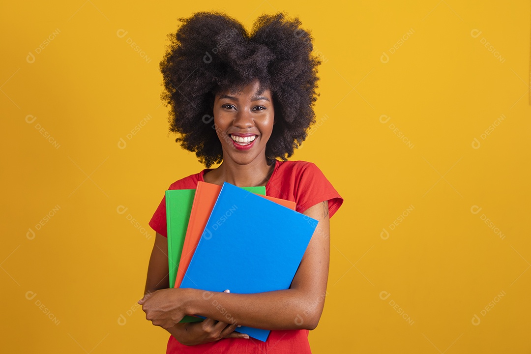 Mulher negra sorridente usando uma camiseta vermelha e segurando cadernos coloridos