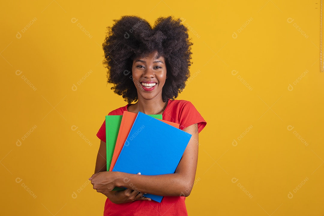 Mulher negra sorridente usando uma camiseta vermelha e segurando cadernos coloridos