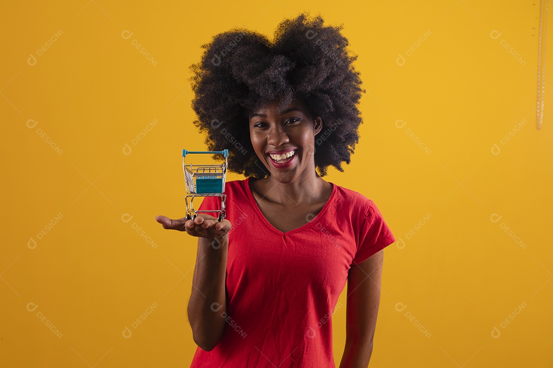 Mulher negra sorridente usando uma camiseta vermelha e segurando um carrinho de compras