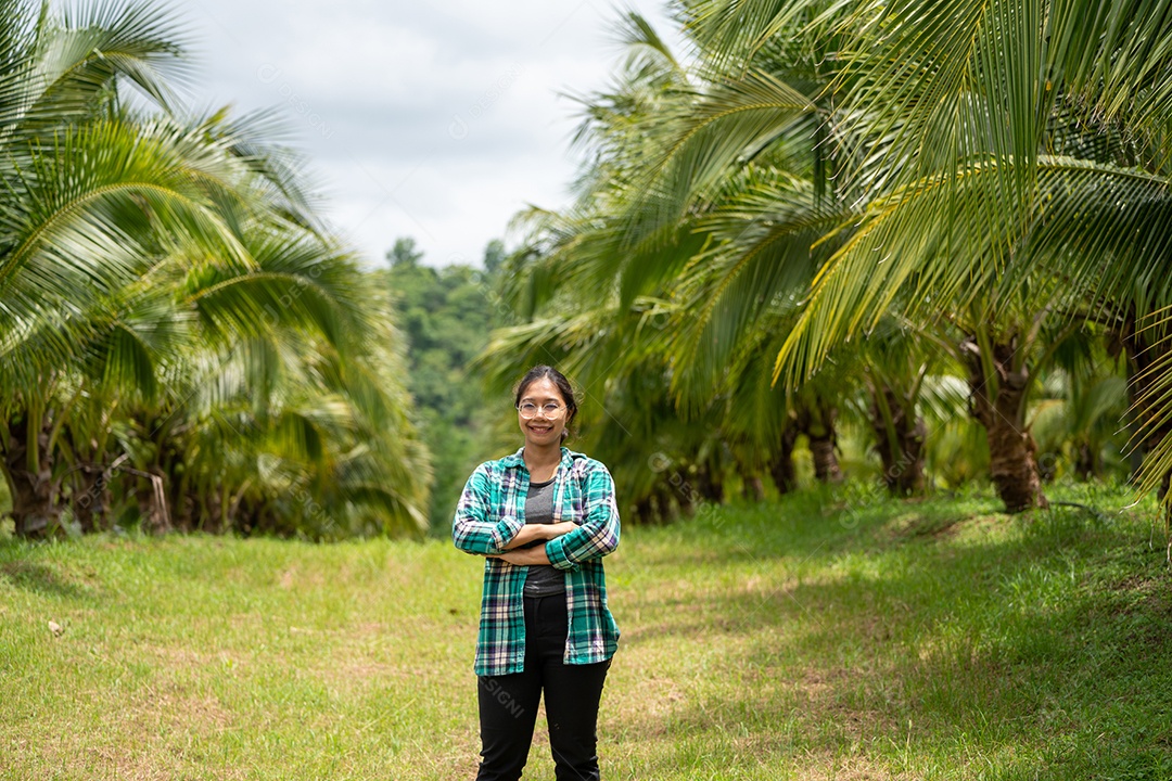 Mulher agricultora de coco cruza o braço no fundo de plantas agrícolas de coqueiros