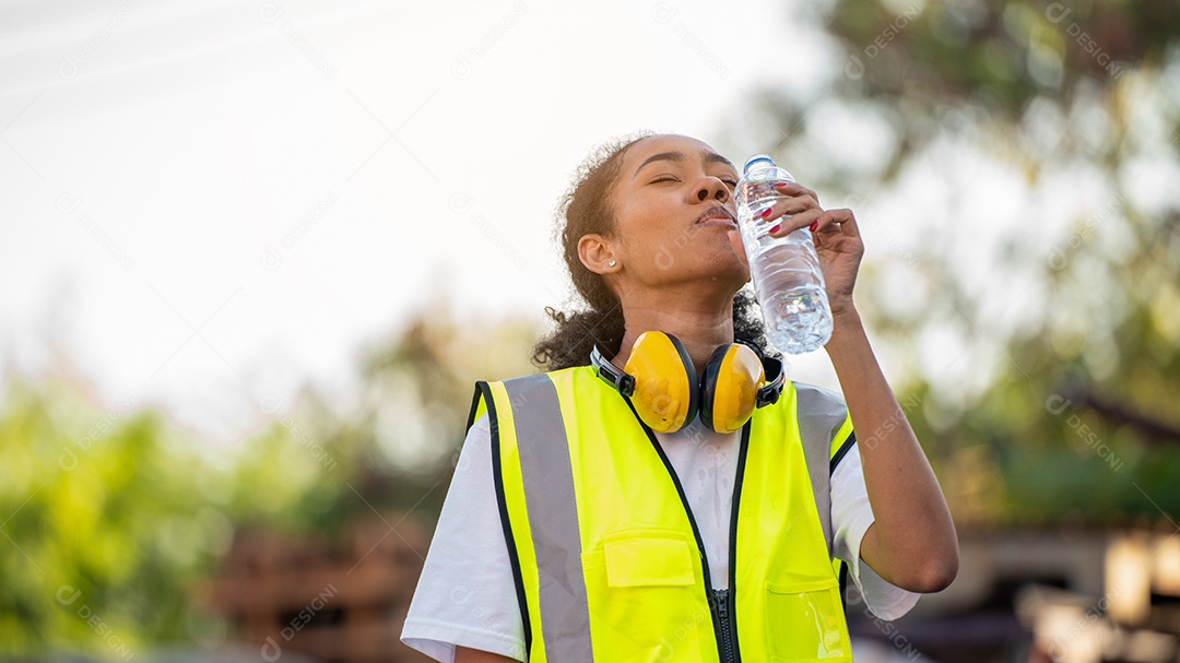 Divergente Um capataz ou trabalhadora afro-americana usando segurança Cross Eye está bebendo uma garrafa de água depois de terminar o trabalho