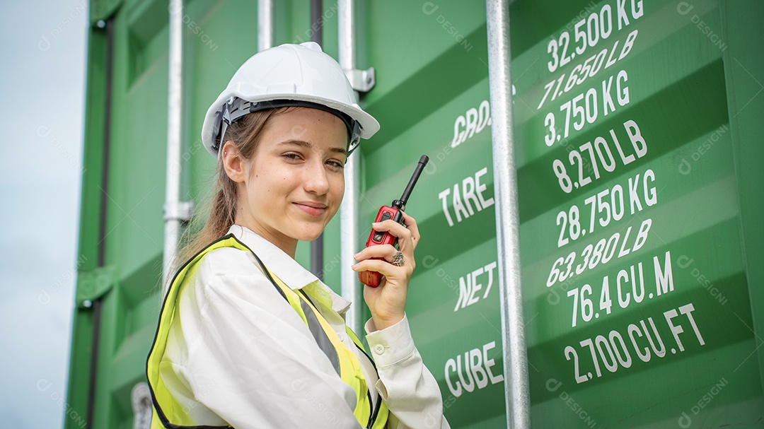 Mulher capataz sorri ao lado do contêiner de carga no armazém, gerente no capacete branco Supervisora