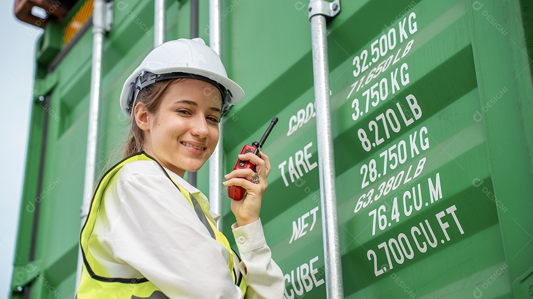 Mulher capataz sorri ao lado do contêiner de carga no armazém, gerente no capacete branco Supervisora