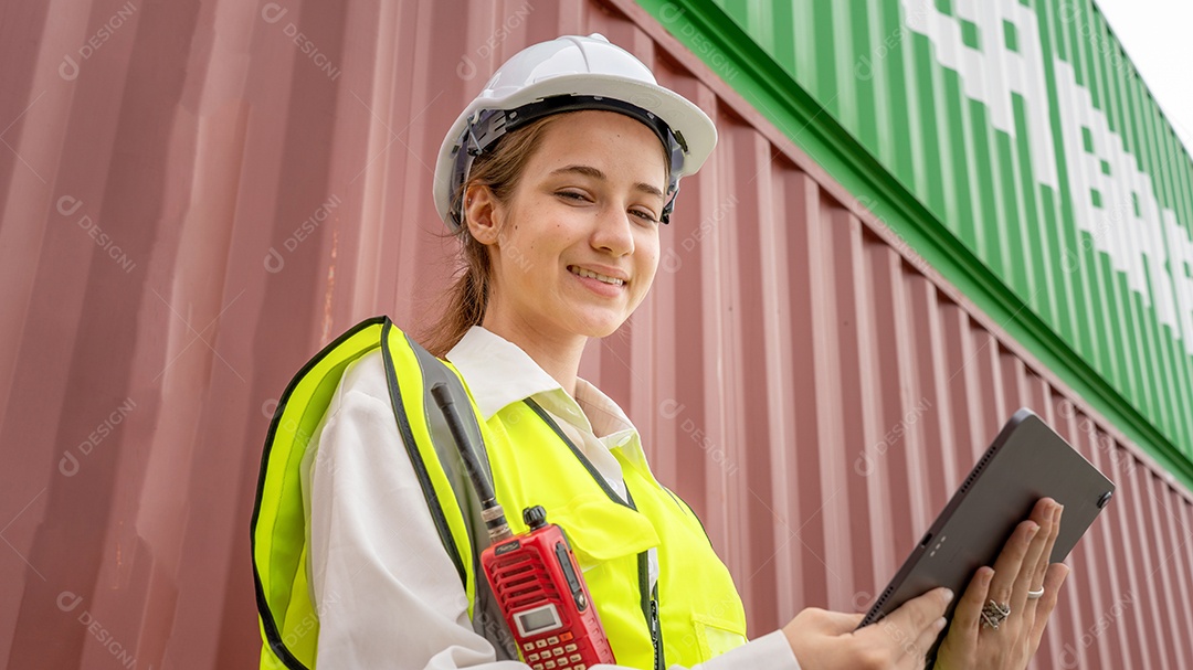 Mulher capataz sorri ao lado da empilhadeira de carga no armazém, gerente usa tablet no capacete branco Supervisor de segurança no conceito de porta do terminal personalizado de contêiner importação exportação