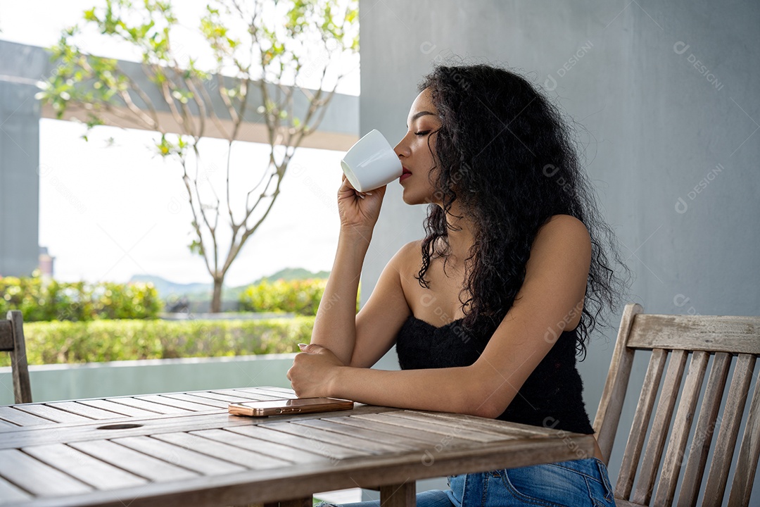 Jovem mulher bebendo uma xícara de café com um sorriso no rosto de pé e sorrindo com um sorriso confiante.