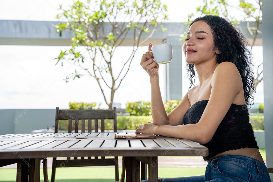 Jovem mulher bebendo uma xícara de café com um sorriso no rosto de pé e sorrindo com um sorriso confiante.