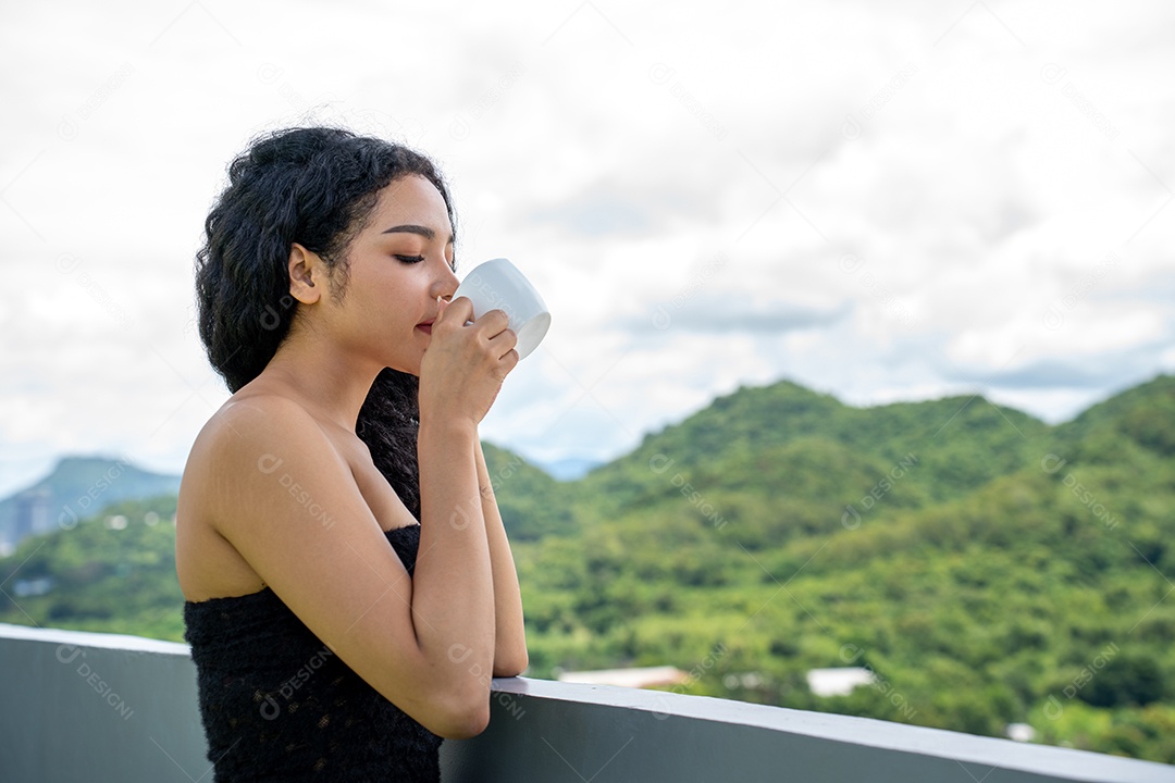 Jovem mulher bebendo uma xícara de café com um sorriso no rosto de pé e sorrindo com um sorriso confiante.