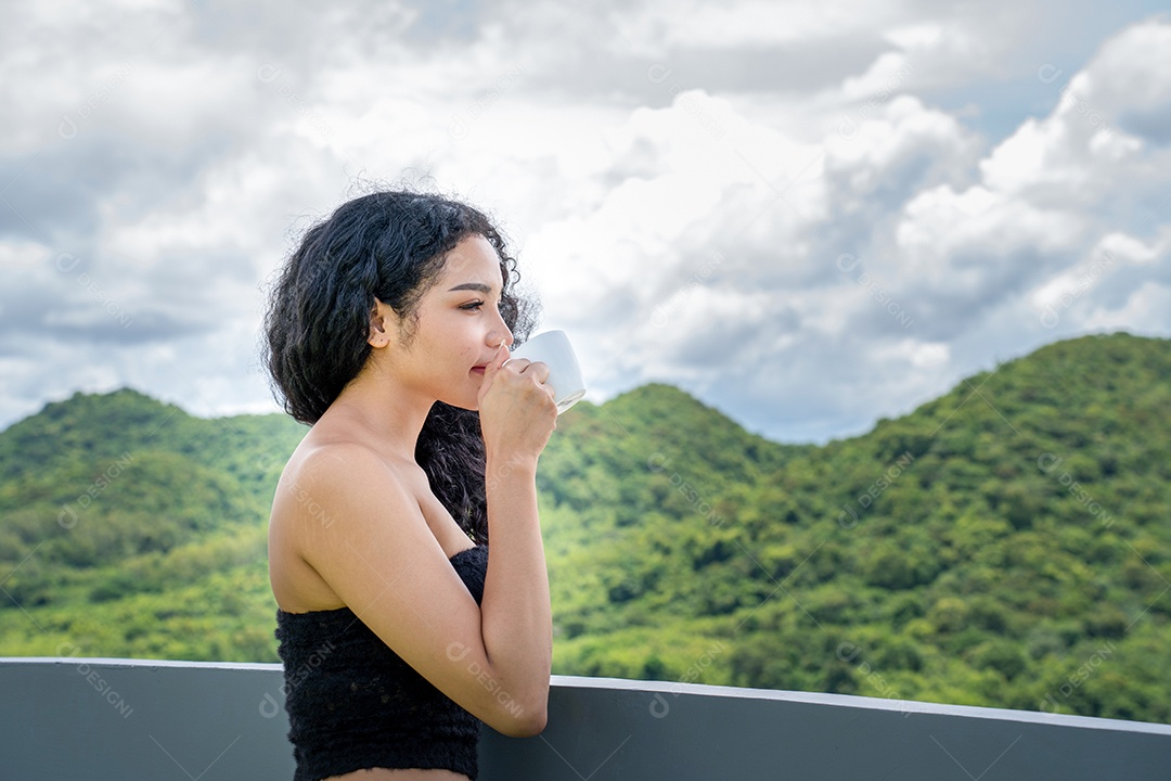 Jovem mulher bebendo uma xícara de café com um sorriso no rosto de pé e sorrindo com um sorriso confiante.