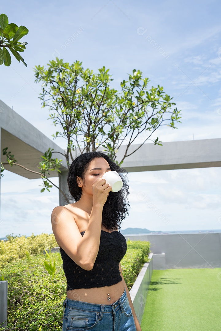 Jovem mulher bebendo uma xícara de café com um sorriso no rosto de pé e sorrindo com um sorriso confiante.