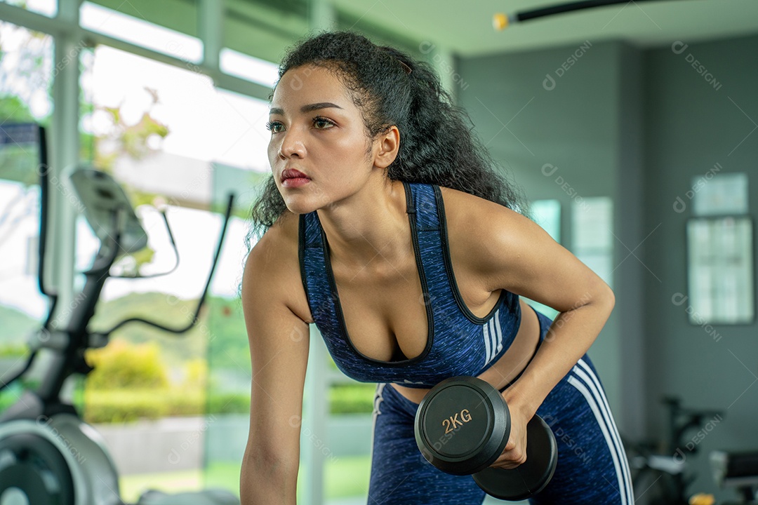Linda jovem musculação com halteres no ginásio.