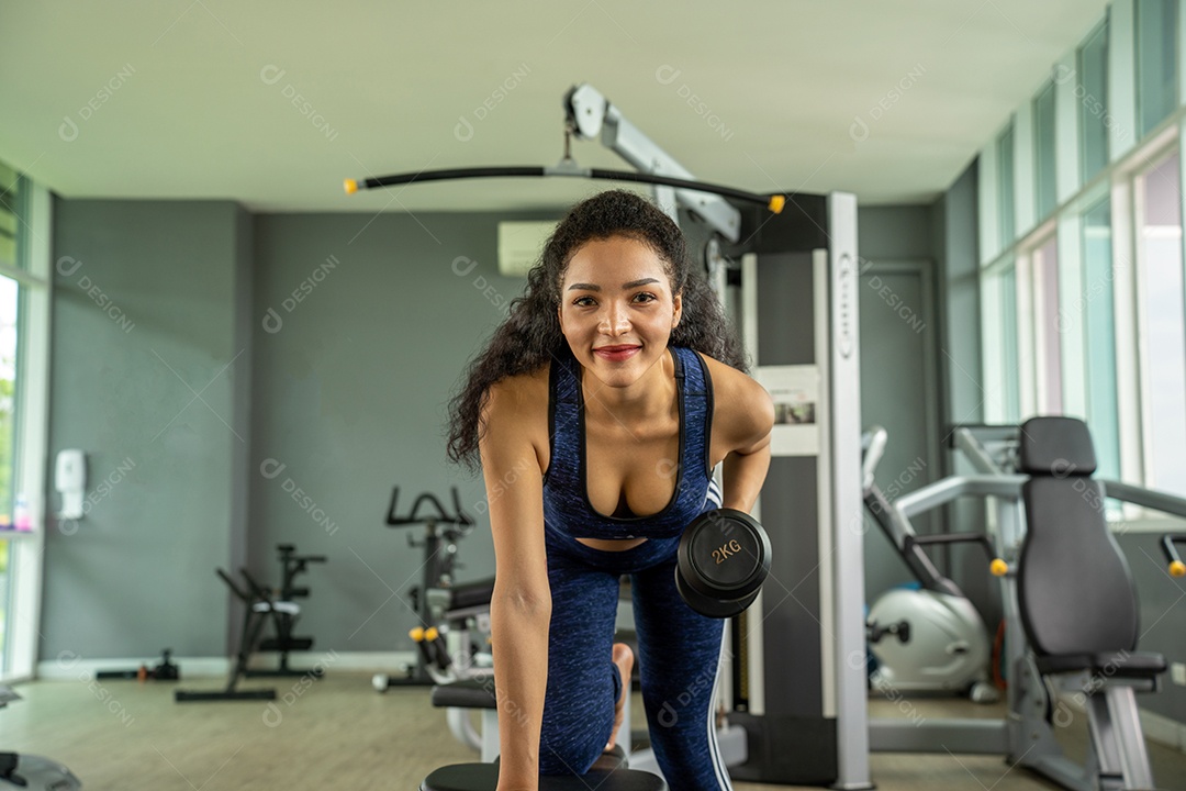 Linda jovem musculação com halteres no ginásio.
