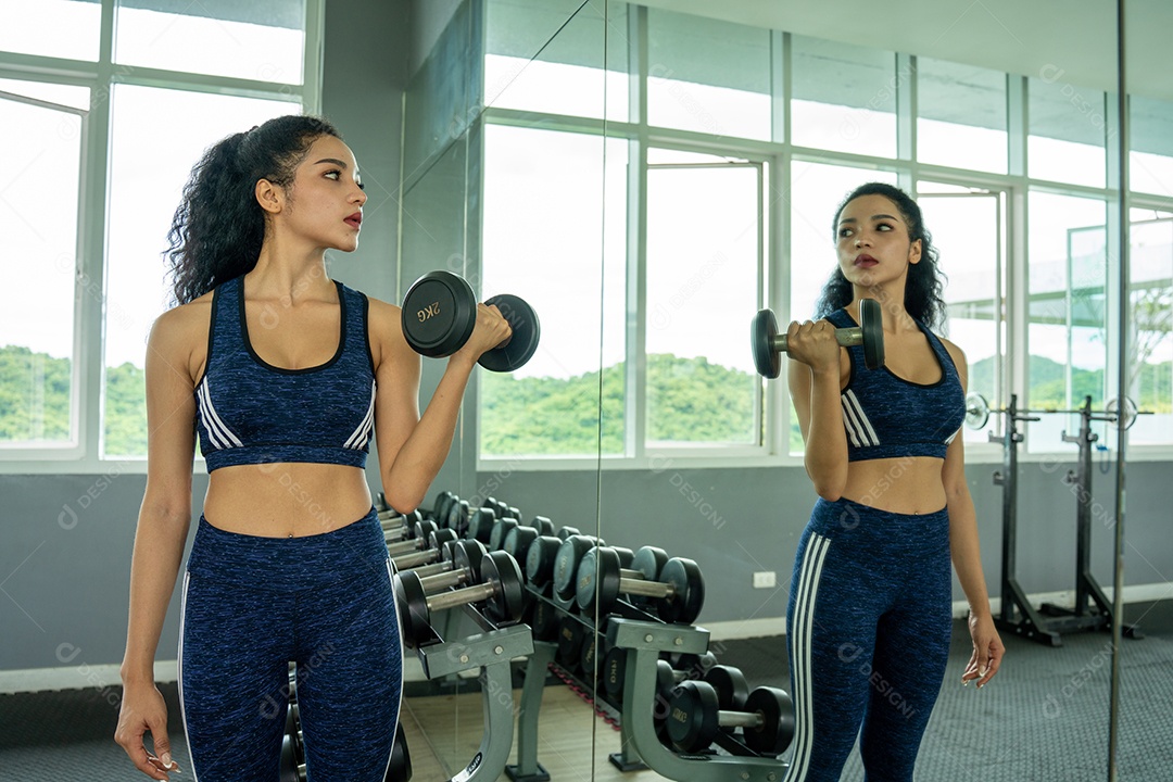 Linda jovem musculação com halteres no ginásio.