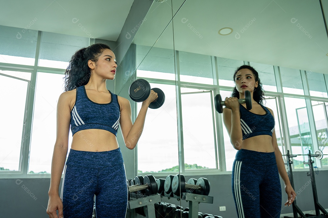Linda jovem musculação com halteres no ginásio.