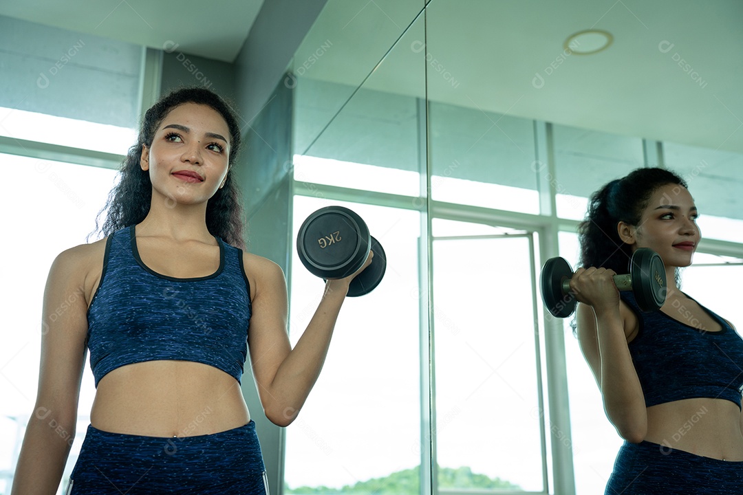 Linda jovem musculação com halteres no ginásio.