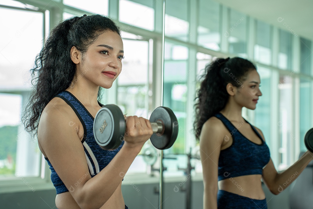 Linda jovem musculação com halteres no ginásio.