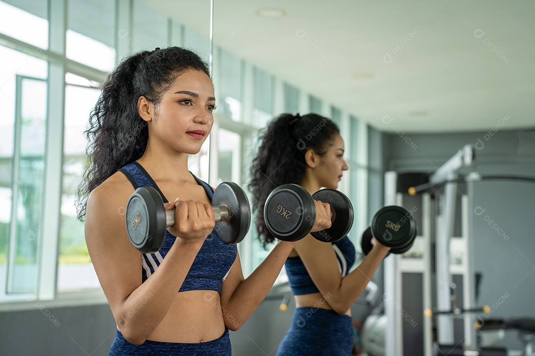 Linda jovem musculação com halteres no ginásio.