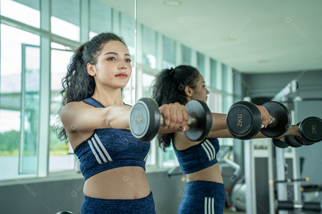 Linda jovem musculação com halteres no ginásio.