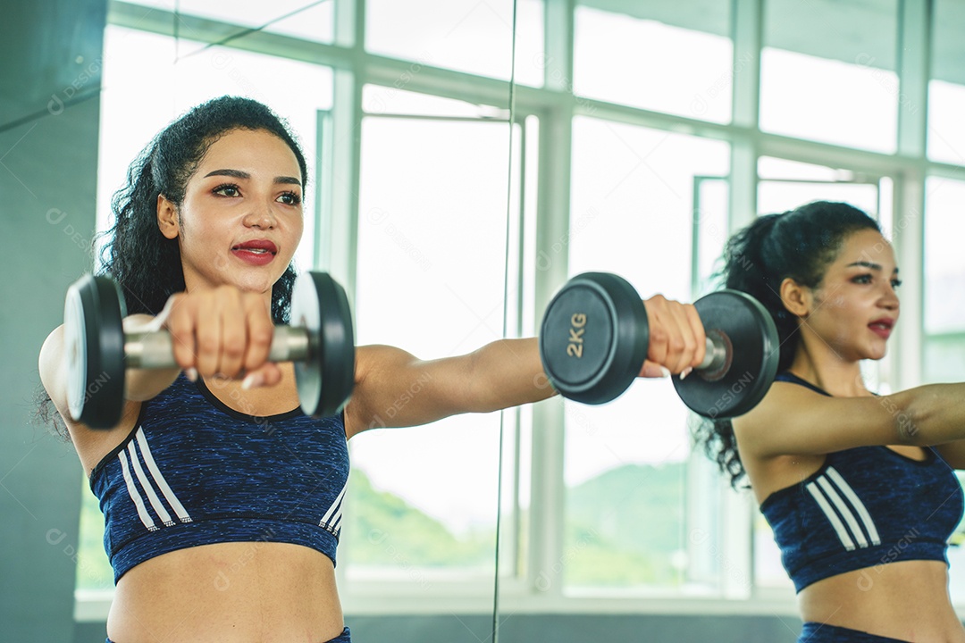 Linda jovem musculação com halteres no ginásio.