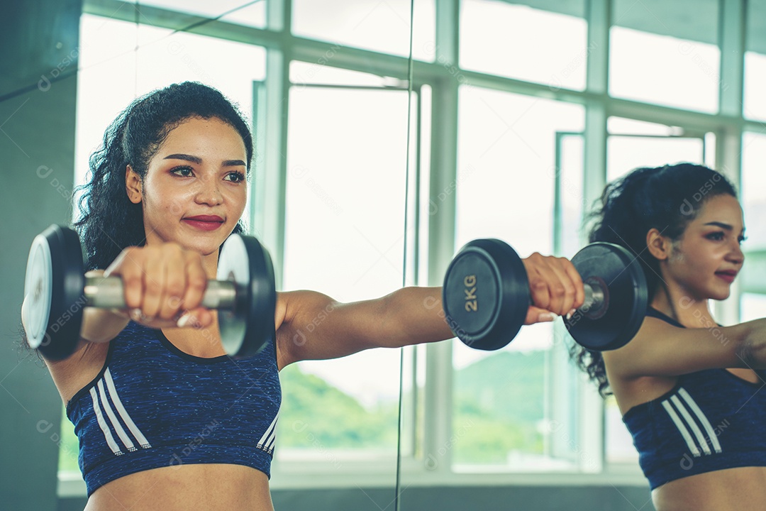 Linda jovem musculação com halteres no ginásio.