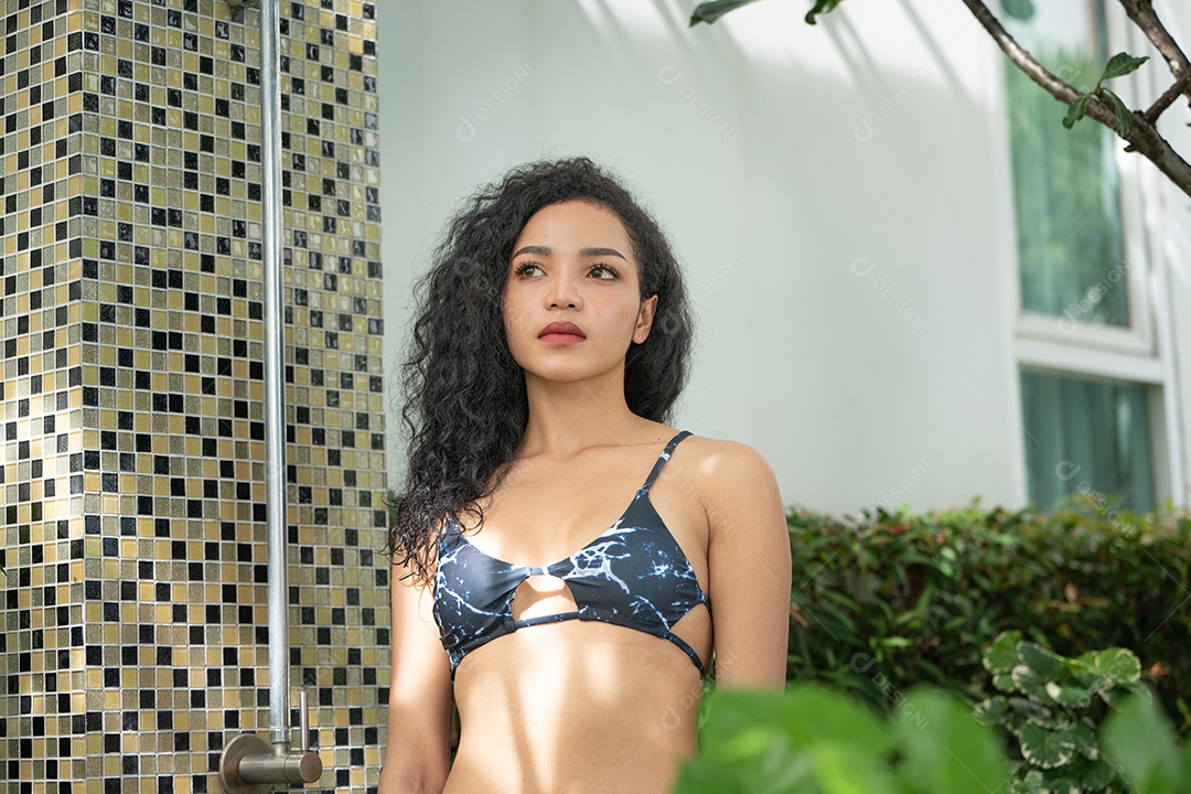 Mulher de biquíni tomando banho depois de nadar na piscina.  Jovem refrescante no chuveiro perto da piscina.