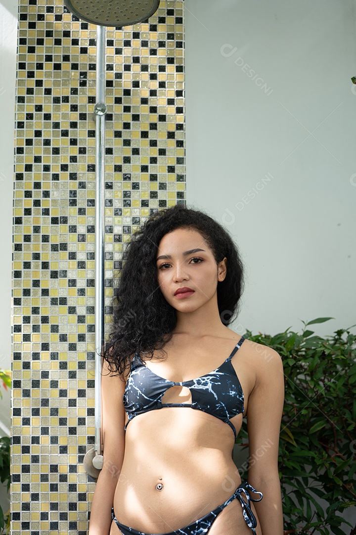 Mulher de biquíni tomando banho depois de nadar na piscina. Jovem refrescante no chuveiro perto da piscina.