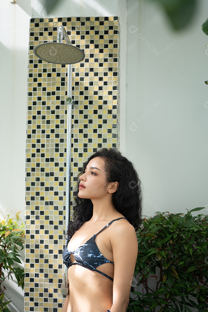 Mulher de biquíni tomando banho depois de nadar na piscina. Jovem refrescante no chuveiro perto da piscina.