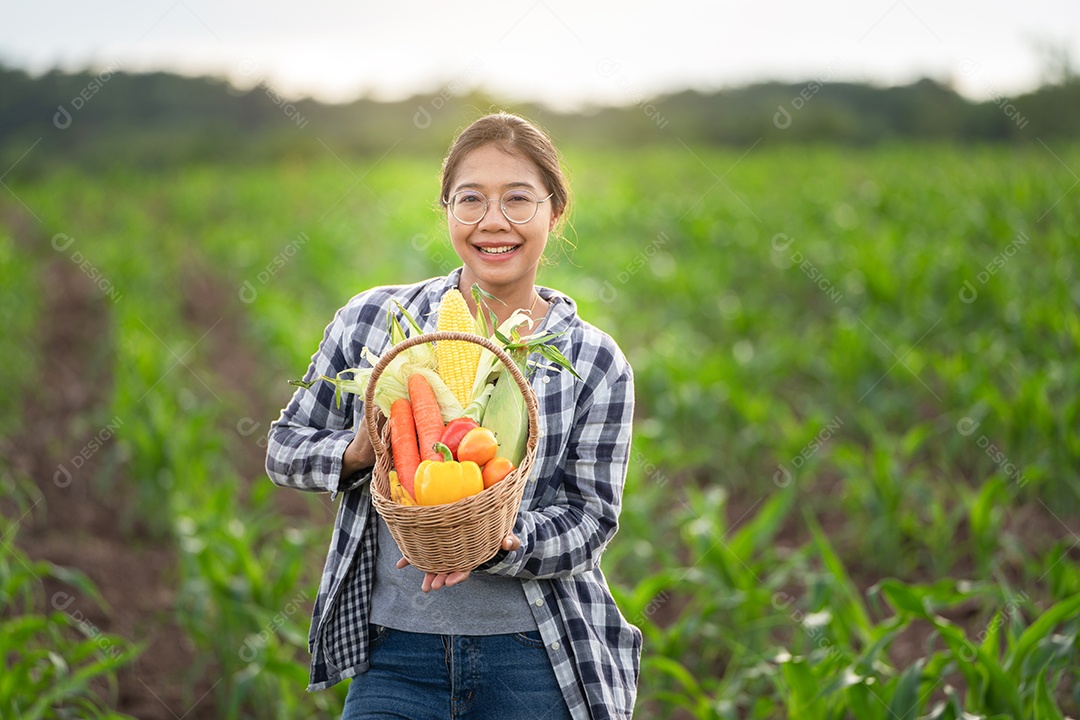 Beautiful young brunette portrait woman hand holding vegetables in bamboo basket on green growing plant on sunset background.