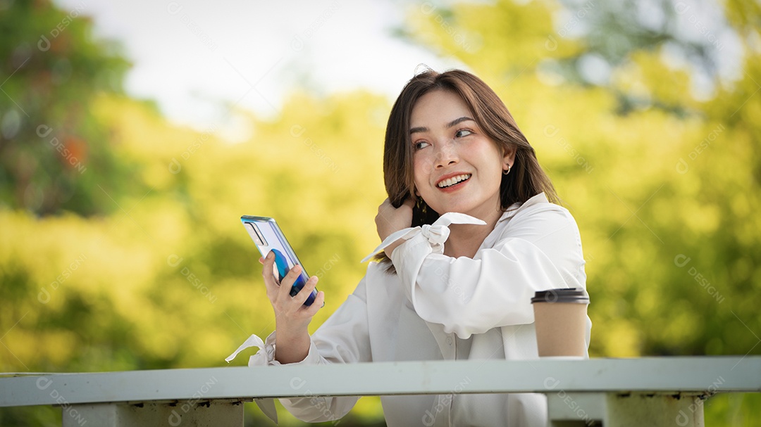 Mulher de sorriso pensativo no parque usando telefone inteligente.