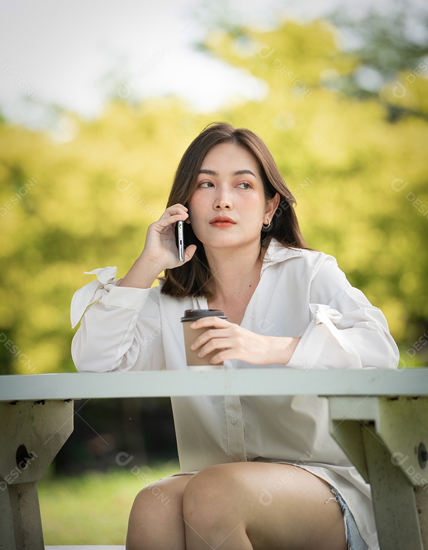 Mulher de sorriso pensativo no parque usando telefone inteligente.