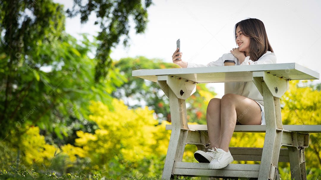 Mulher de sorriso pensativo no parque usando telefone inteligente.