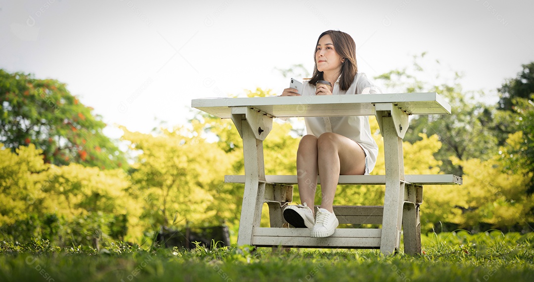 Mulher de sorriso pensativo no parque usando telefone inteligente.