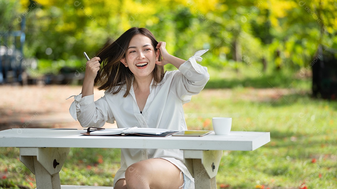 Mulher de sorriso pensativo no parque usando notebook e escrevendo.