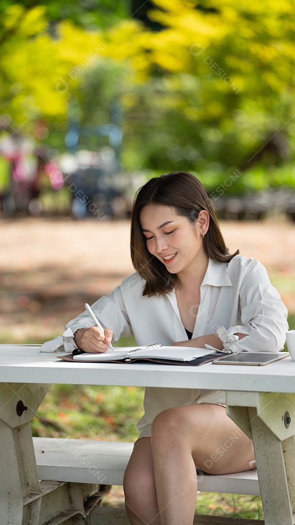 Mulher de sorriso pensativo no parque usando notebook e escrevendo.