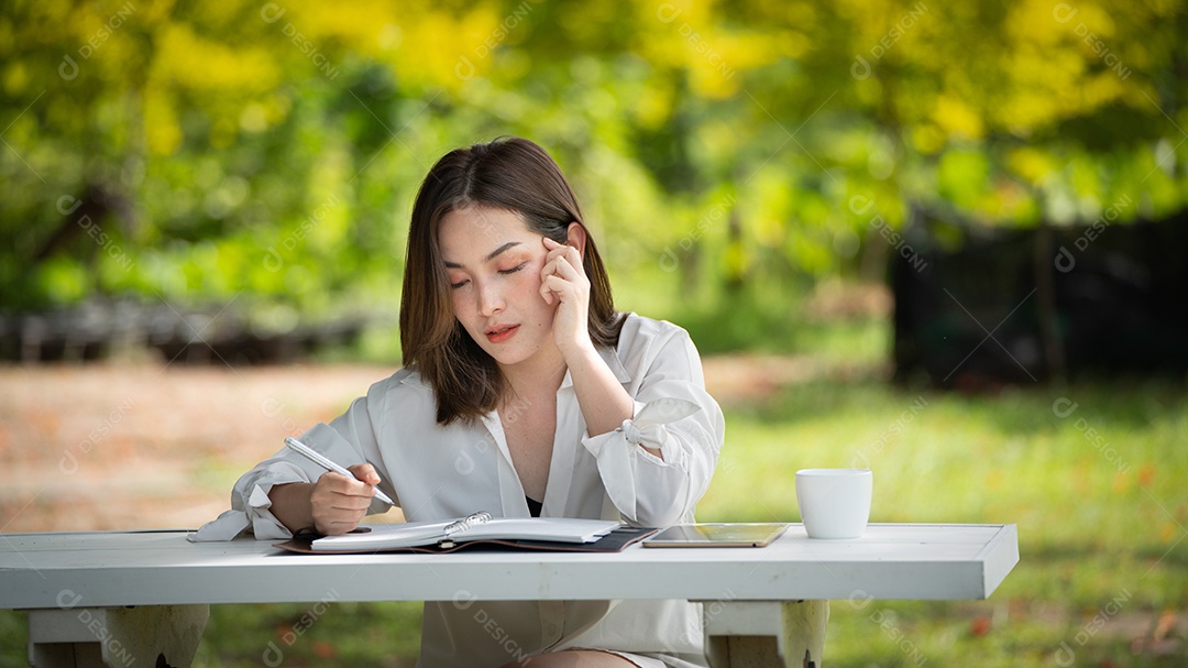 Mulher de sorriso pensativo no parque usando notebook e escrevendo.
