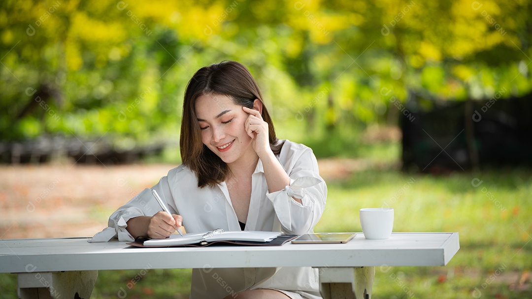 Mulher de sorriso pensativo no parque usando notebook e escrevendo.