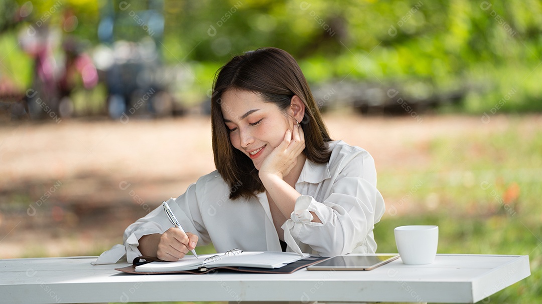 Mulher de sorriso pensativo no parque usando notebook e escrevendo.