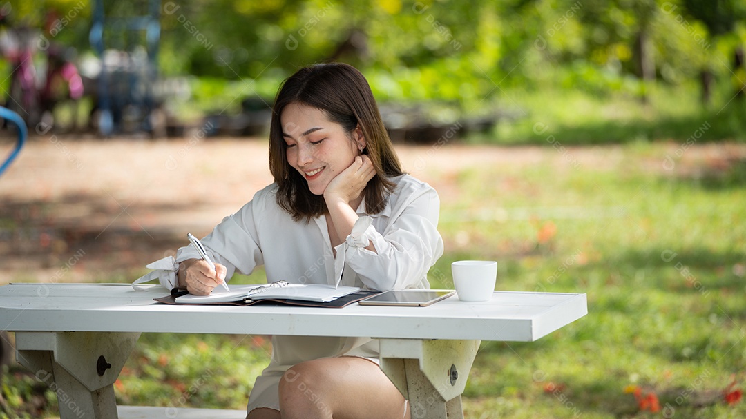 Mulher de sorriso pensativo no parque usando notebook e escrevendo.