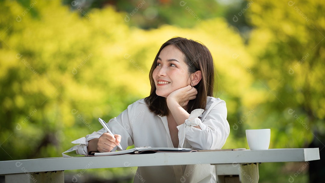 Mulher de sorriso pensativo no parque usando notebook e escrevendo.