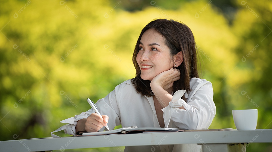 Mulher de sorriso pensativo no parque usando notebook e escrevendo.