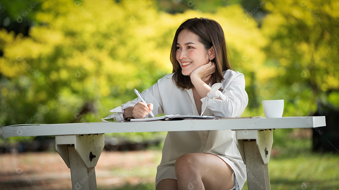 Mulher de sorriso pensativo no parque usando notebook e escrevendo.
