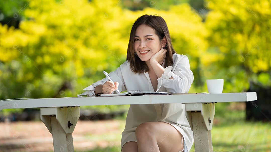 Mulher de sorriso pensativo no parque usando notebook e escrevendo.